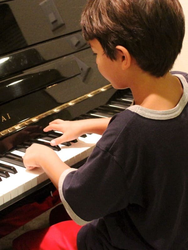 Un petit garçon jouant du piano après avoir pris des cours de piano dans l'école de musique Groove Lab